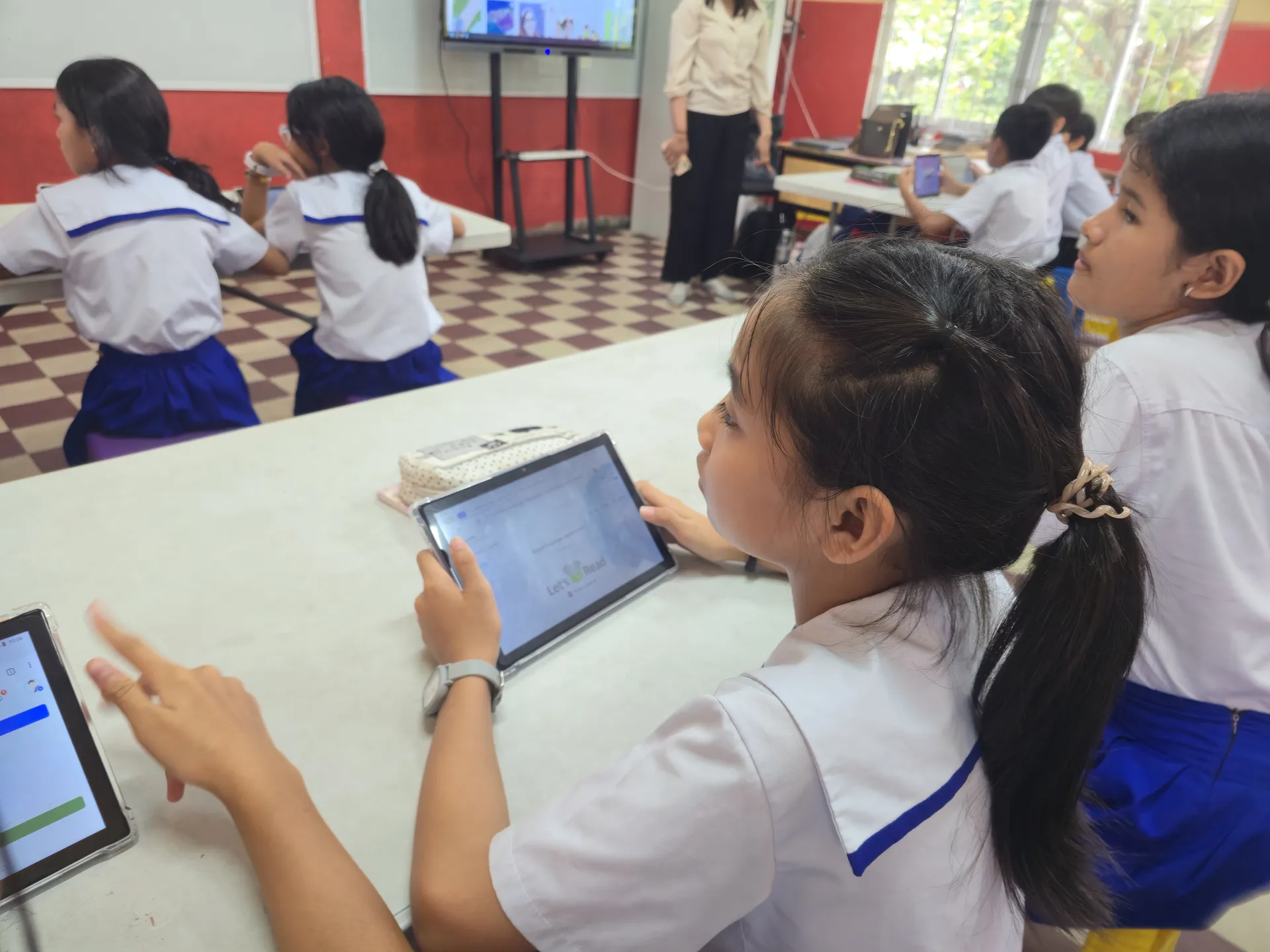 A student opening the reading app on a tablet while the teacher projects it at the front of the class.