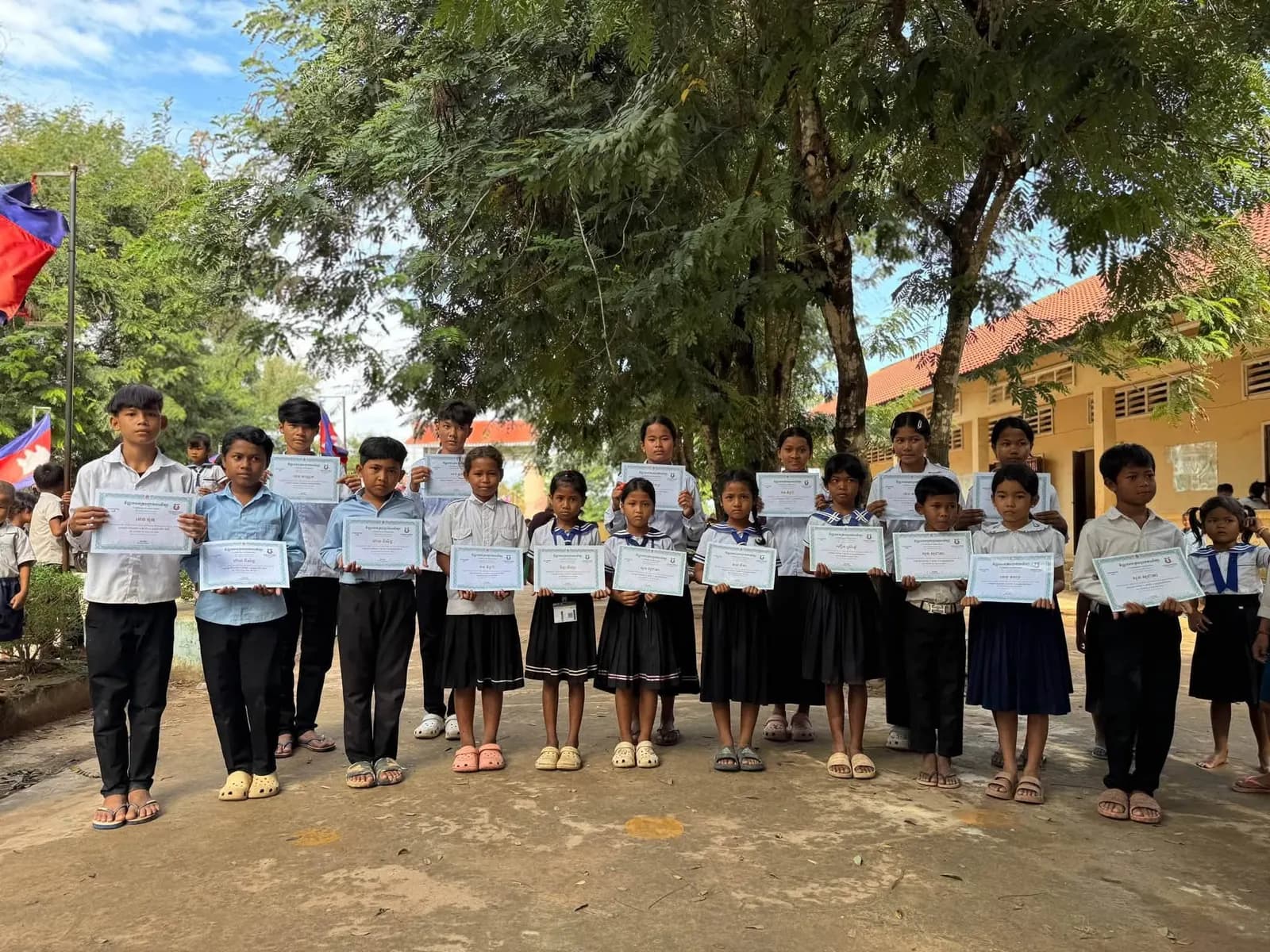 A line of primary school students standing in a schoolyard holding completion certificates.